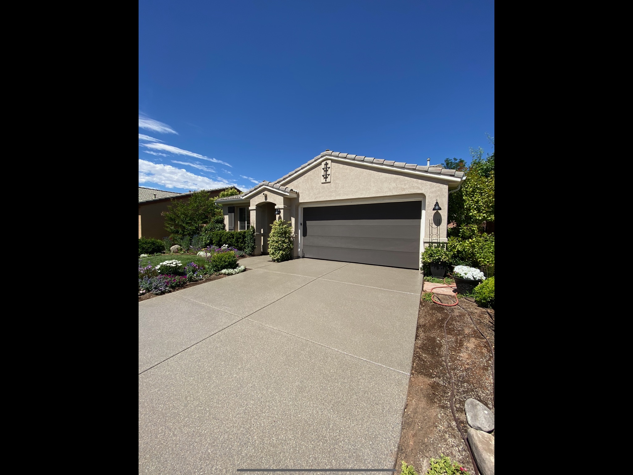 Wide tan driveway coating with lush garden landscape - Sparks Coatings